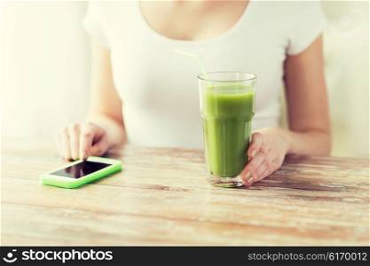 healthy eating, diet, detox, technology and people concept - close up of woman with smartphone green juice sitting at wooden table