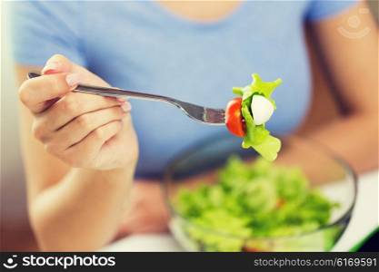 healthy eating, diet, food and people concept - close up of young woman eating vegetable salad with fork at home