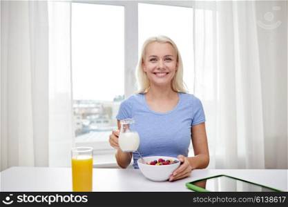 healthy eating, diet, lifestyle and people concept - smiling young woman with milk and cornflakes having breakfast at home