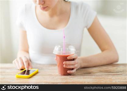 healthy eating, diet, technology and people concept - close up of woman with smartphone and cup of smoothie sitting at table