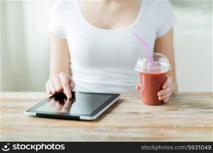 healthy eating, diet, technology and people concept - close up of woman hands with tablet pc computer and cup of smoothie sitting at table