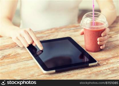 healthy eating, diet, technology and people concept - close up of woman hands with cup of smoothie pointing finger to tablet pc computer black blank screen on wooden table