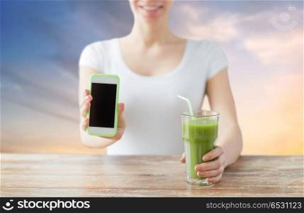 healthy eating, diet, technology and people concept - close up of woman with smartphone and green juice sitting at wooden table over sky background. close up of woman with smartphone and green juice. close up of woman with smartphone and green juice
