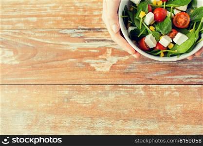 healthy eating, dieting and people concept - close up of young woman hands with salad bowl on blank table at home