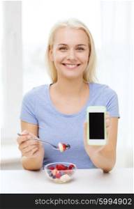 healthy eating, dieting and people concept - smiling young woman eating fruit salad and showing blank smartphone screen at home