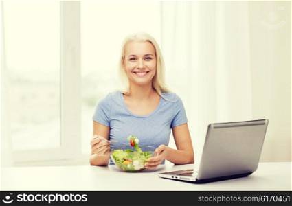 healthy eating, dieting and people concept - smiling young woman with laptop computer eating vegetable salad at home