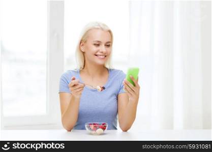 healthy eating, dieting and people concept - smiling young woman with smartphone eating fruit salad at home
