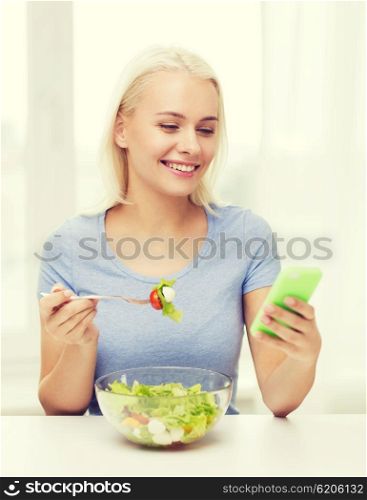 healthy eating, dieting and people concept - smiling young woman with smartphone eating vegetable salad at home