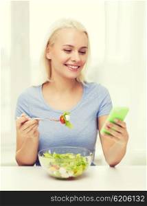 healthy eating, dieting and people concept - smiling young woman with smartphone eating vegetable salad at home