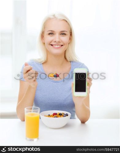 healthy eating, dieting and people concept - smiling young woman with tablet pc computer eating breakfast and showing blank smartphone screen at home
