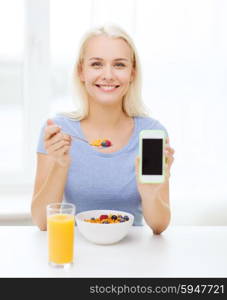 healthy eating, dieting and people concept - smiling young woman with tablet pc computer eating breakfast and showing blank smartphone screen at home