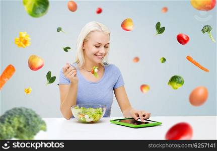 healthy eating, dieting and people concept - smiling young woman with tablet pc computer eating vegetable salad over gray background with falling vegetables