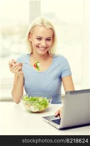 healthy eating, dieting, food, technology and people concept - smiling young woman with laptop computer eating vegetable salad at home