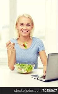 healthy eating, dieting, food, technology and people concept - smiling young woman with laptop computer eating vegetable salad at home