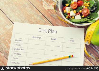 healthy eating, dieting, slimming and weigh loss concept - close up of diet plan paper green apple, measuring tape and salad