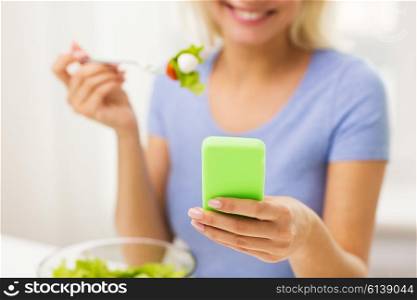 healthy eating, dieting, technology, food and people concept - close up of smiling young woman with smartphone eating vegetable salad at home