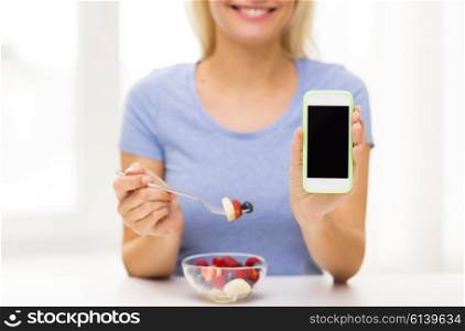 healthy eating, dieting, technology, food and people concept - close up of young woman with smartphone eating fruit salad at home