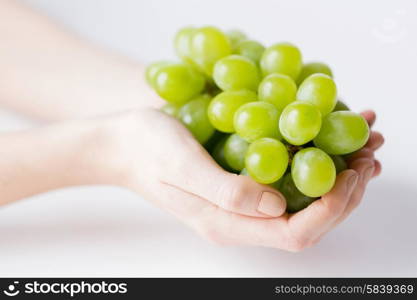 healthy eating, dieting, vegetarian food and people concept - close up of woman hands holding green grape bunch at home