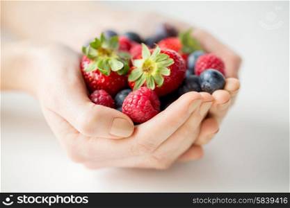 healthy eating, dieting, vegetarian food and people concept - close up of woman hands holding berries at home