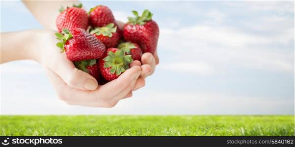 healthy eating, dieting, vegetarian food and people concept - close up of woman hands holding ripe strawberries over grass and blue sky background