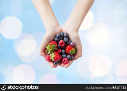 healthy eating, dieting, vegetarian food and people concept - close up of woman hands holding different ripe summer berries over blue lights background