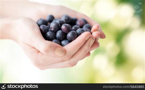 healthy eating, dieting, vegetarian food and people concept - close up of woman hands holding ripe blueberries over green natural background