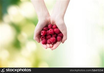 healthy eating, dieting, vegetarian food and people concept - close up of woman hands holding ripe raspberries over green natural background