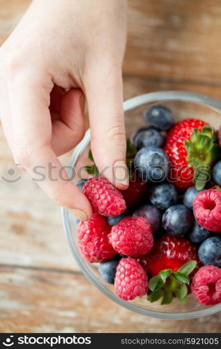 healthy eating, dieting, vegetarian food and people concept - close up of woman hands with berries mix in glass bowl on wooden table