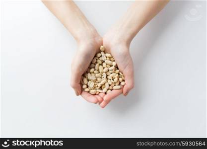 healthy eating, dieting, vegetarian food and people concept - close up of woman hands holding peeled peanuts at home