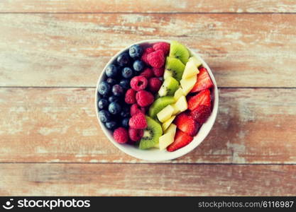 healthy eating, dieting, vegetarian food and people concept - close up of fruits and berries in bowl on wooden table