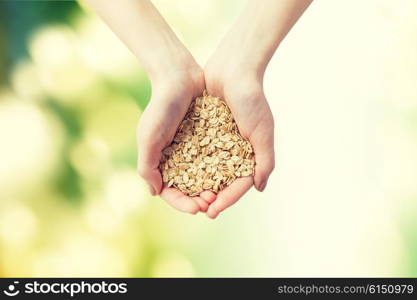 healthy eating, dieting, vegetarian food and people concept - close up of woman hands holding oatmeal flakes over green natural background