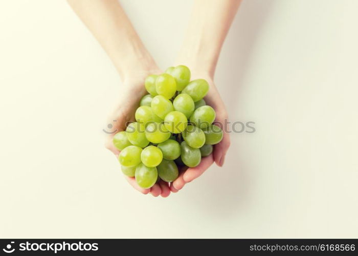 healthy eating, dieting, vegetarian food and people concept - close up of woman hands holding green grape bunch at home