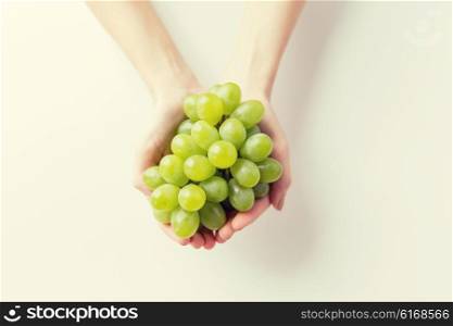 healthy eating, dieting, vegetarian food and people concept - close up of woman hands holding green grape bunch at home