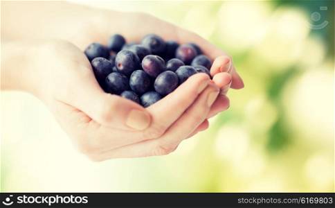 healthy eating, dieting, vegetarian food and people concept - close up of woman hands holding ripe blueberries over green natural background