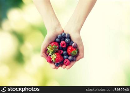 healthy eating, dieting, vegetarian food and people concept - close up of woman hands holding different ripe summer berries over green natural background