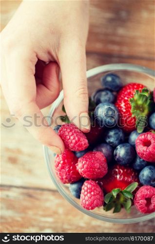 healthy eating, dieting, vegetarian food and people concept - close up of woman hands with berries mix in glass bowl on wooden table