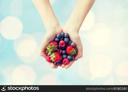 healthy eating, dieting, vegetarian food and people concept - close up of woman hands holding different ripe summer berries over blue lights background