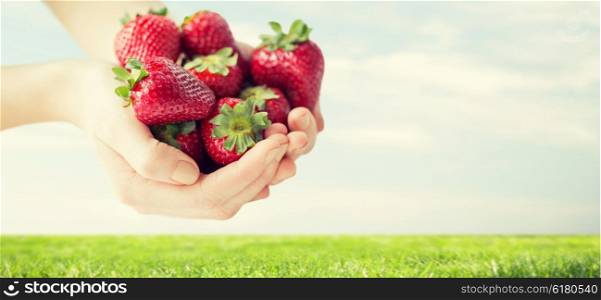 healthy eating, dieting, vegetarian food and people concept - close up of woman hands holding ripe strawberries over grass and blue sky background