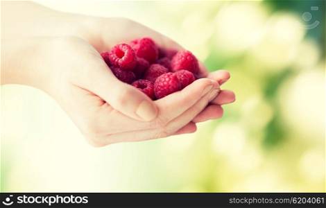 healthy eating, dieting, vegetarian food and people concept - close up of woman hands holding raspberries over green natural background
