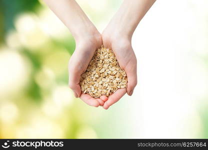 healthy eating, dieting, vegetarian food and people concept - close up of woman hands holding oatmeal flakes over green natural background