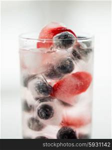 healthy eating, drinks, diet and detox concept - close up of fruit water with strawberry, blackcurrant or blueberry and ice cubes in glass