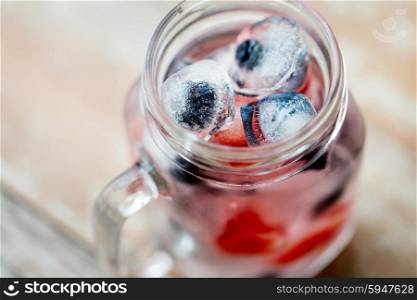 healthy eating, drinks, diet and detox concept - close up of fruit water with strawberry, blackcurrant or blueberry and ice cubes in glass mug on table