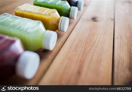 healthy eating, drinks, diet and detox concept - close up of plastic bottles with different fruit or vegetable juices on wooden table