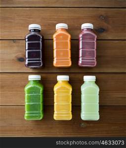 healthy eating, drinks, diet and detox concept - close up of plastic bottles with different fruit or vegetable juices on wooden table