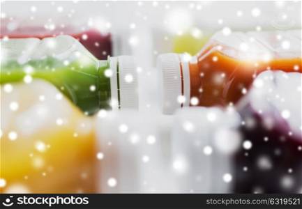 healthy eating, drinks, diet and detox concept - close up of plastic bottles with different fruit or vegetable juices on white over snow. bottles with different fruit or vegetable juices