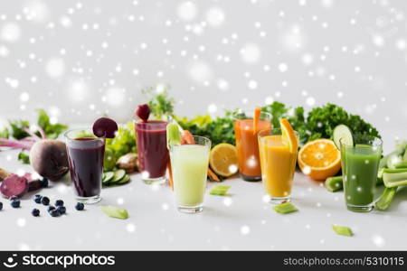 healthy eating, drinks, diet and detox concept - glasses with different fruit or vegetable juices and food on table over snow. glasses with different fruit or vegetable juices