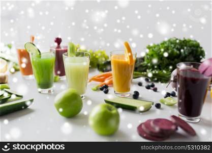healthy eating, drinks, diet and detox concept - glasses with different fruit or vegetable juices and food on table over snow. glasses with different fruit or vegetable juices