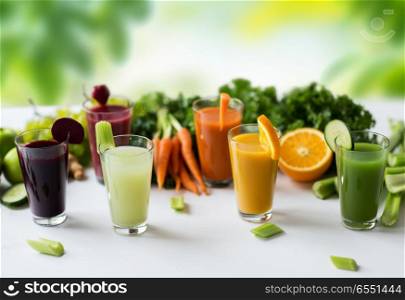 healthy eating, drinks, diet and detox concept - glasses with different fruit or vegetable juices and food on table over green natural background. glasses with different fruit or vegetable juices. glasses with different fruit or vegetable juices