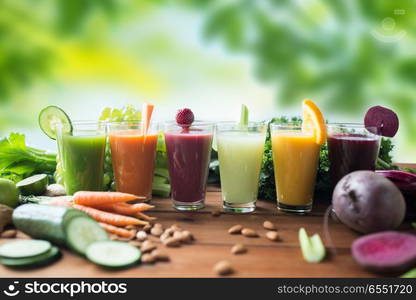 healthy eating, drinks, diet and detox concept - glasses with different fruit or vegetable juices and food on table over green natural background. glasses with different fruit or vegetable juices. glasses with different fruit or vegetable juices