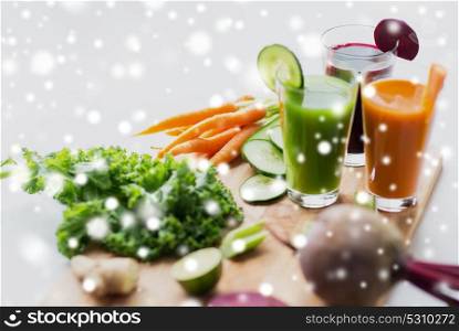 healthy eating, drinks, diet and detox concept - glasses with vegetable fresh juices and food on table over snow. glasses with different vegetable fresh juices